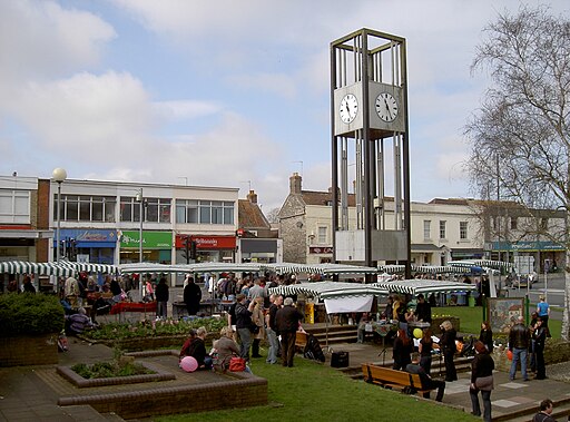 Busy Keynsham Farmers' Market with green and white striped stalls, clock tower and shoppers at Market Walk